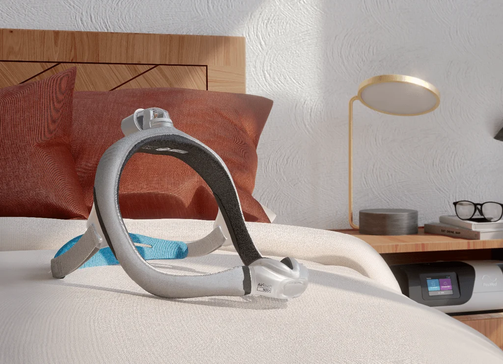 A CPAP mask resting on a bed beside a CPAP machine